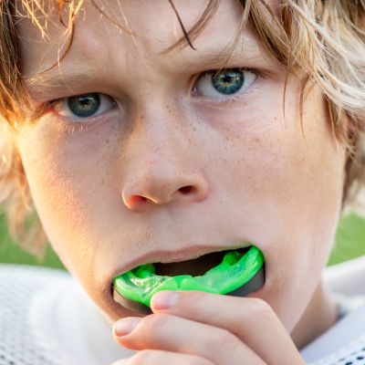 a young athlete boy with blonde hair, putting a green mouthguard in his mouth before a match
