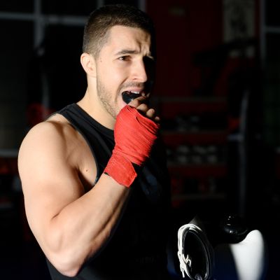 A Boxing fighter with red hand wraps, wearing a black tank top, inserting a mouthguard in a gym setting.