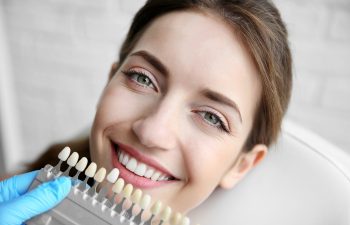 Young woman choosing color of teeth at dentist